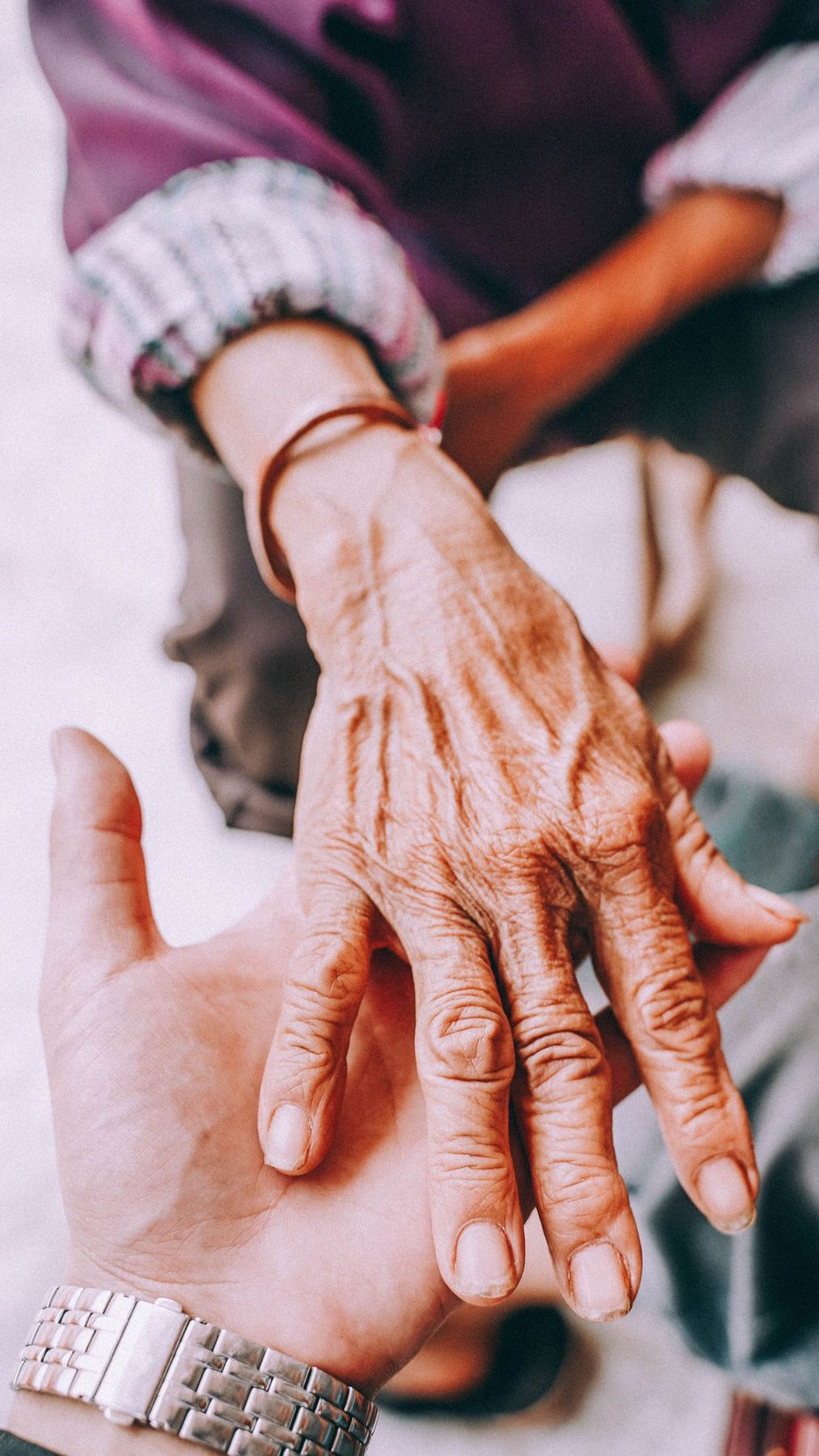An older adult resting a hand in a caregiver's hand