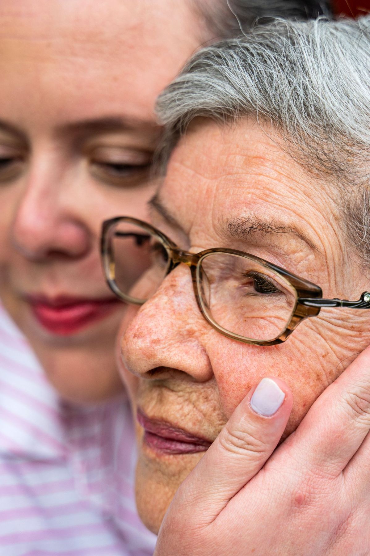 A caregiver hugging a senior woman cheek to cheek